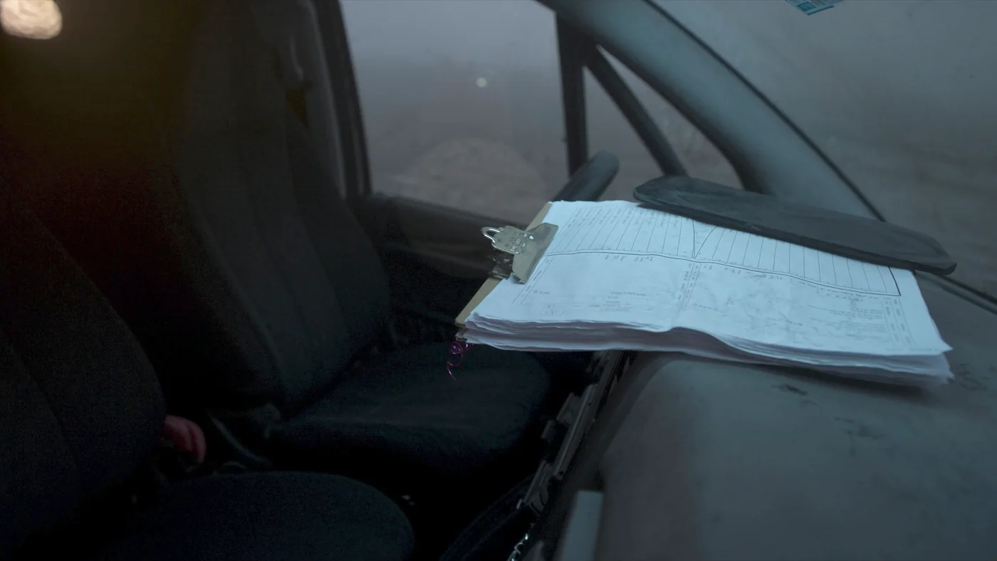 A clipboard of inspection sheets resting on the dashboard of a maintenance van at first light