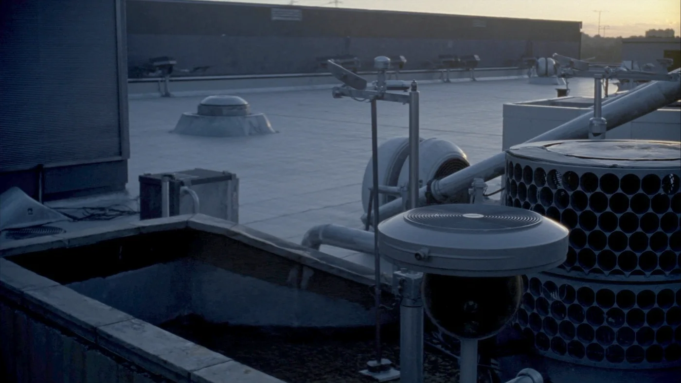 A rooftop of sensors and conduit runs on a flat commercial roof at dawn