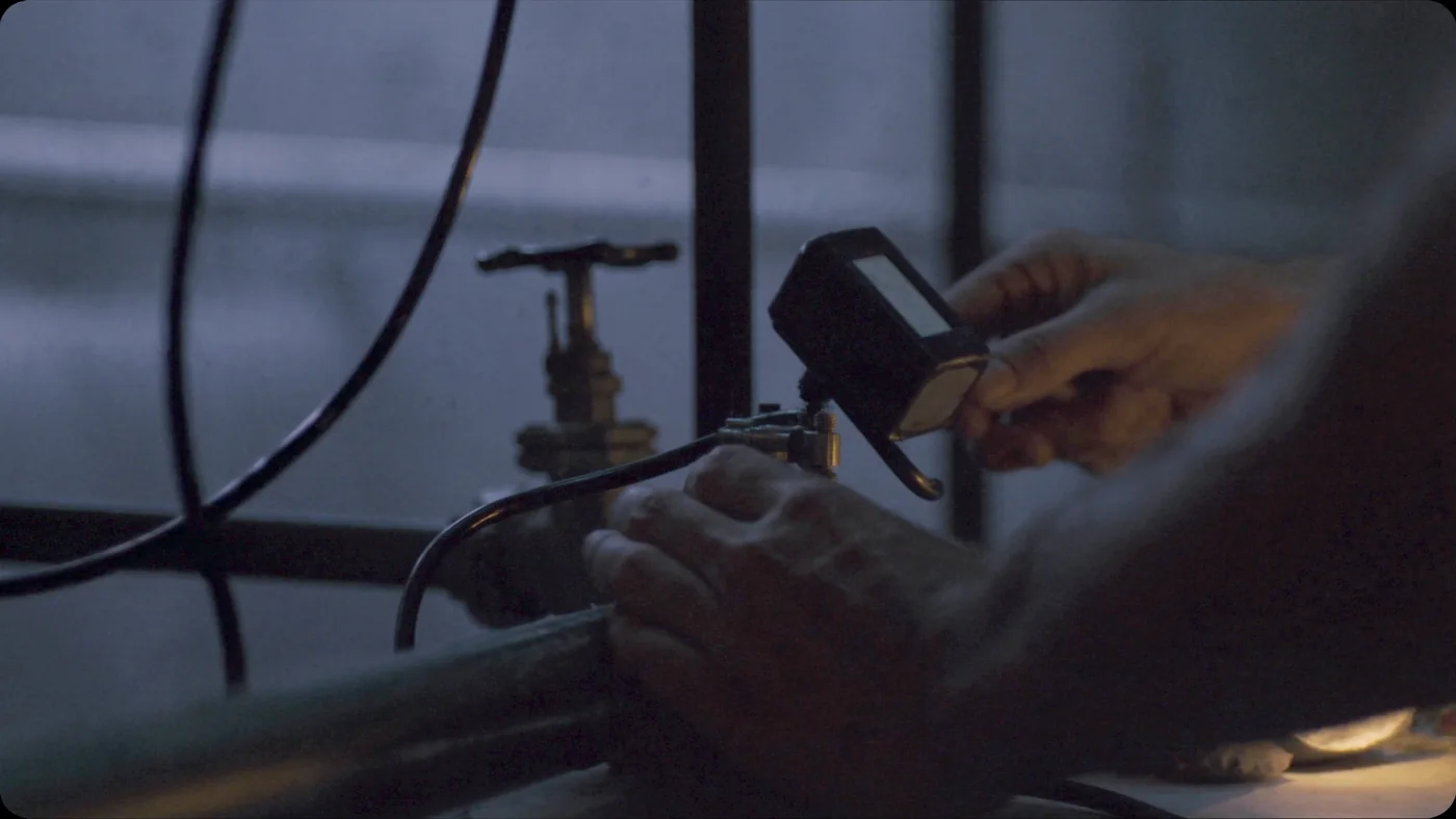 A technician's hands fitting a clamp sensor to a plant room pipe